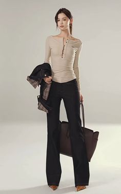 Woman in a long sleeve shirt and dark jeans holding a jacket and a bag