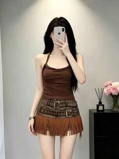 Person with long black hair taking a mirror selfie in a halter top and fringe skirt