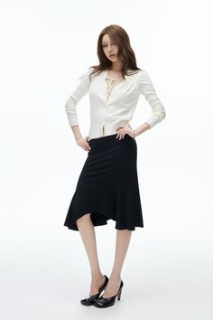 Woman with long hair in a white cardigan and black skirt posing in a studio