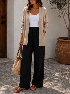 Woman in a beige cardigan and black pants holding a straw bag outdoors