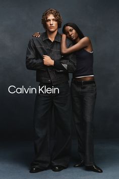 Two people in dark wash denim clothing posing against a dark background