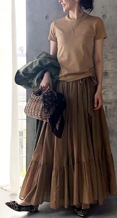 Woman in a brown top and long skirt holding a wicker bag and green jacket