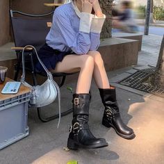 Person in a striped shirt and mini skirt sitting outdoors with black boots and a silver bag