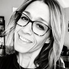 Woman with glasses and short hair smiling in a black and white portrait