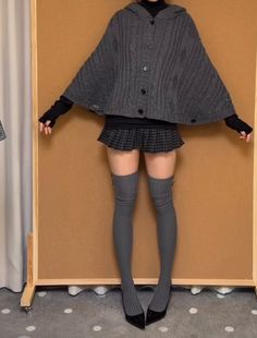 Person wearing a hooded poncho, plaid skirt, and thigh high socks indoors