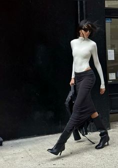 Woman in a white turtleneck and black skirt walking on a street