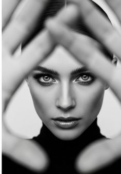 Woman in a black turtleneck with hands framing her face in a black and white portrait