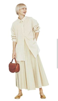 Woman with short blonde hair wearing a long sleeve shirt and pleated skirt