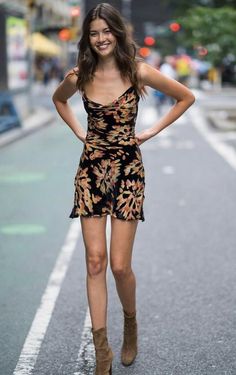 Woman in a floral dress and brown boots standing on a street