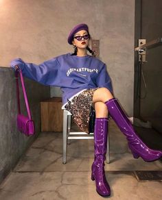 Woman in a purple beret, sequin skirt, and purple boots sitting indoors