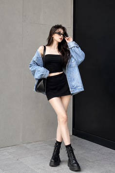 Woman in a denim jacket, black tube top, and mini skirt posing outdoors
