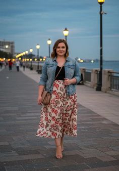 Woman in a denim jacket and floral skirt walking on a promenade at night