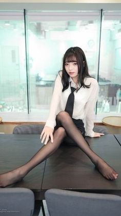 Woman in a white shirt and black tie sitting on a table with legs crossed