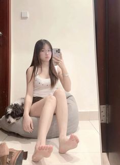 Young woman in glasses taking a mirror selfie while sitting on a beanbag with a dog