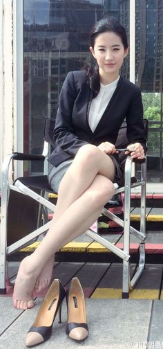 Woman in business attire sitting outdoors with bare feet and high heels on the ground