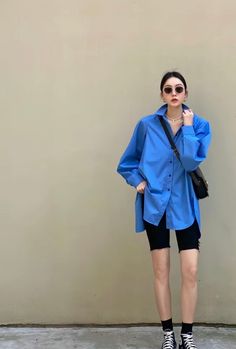 Woman in a blue oversized shirt and black shorts with sunglasses and a shoulder bag