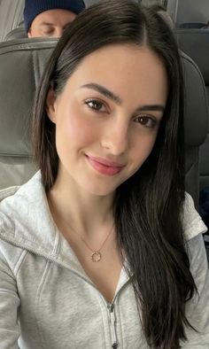 Woman with long dark hair and a gold necklace smiling in a light grey hoodie