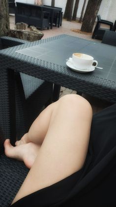 Person with crossed legs and bare feet at an outdoor cafe table with a coffee cup