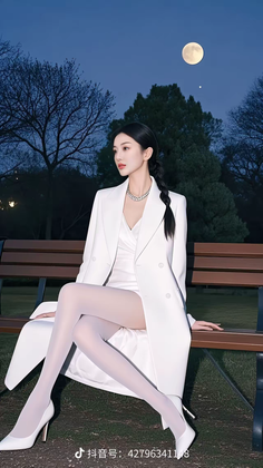 Woman in a white blazer and dress sitting on a bench at night under a full moon