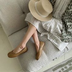Person wearing a straw hat, white dress, and ballet flats sitting on a couch