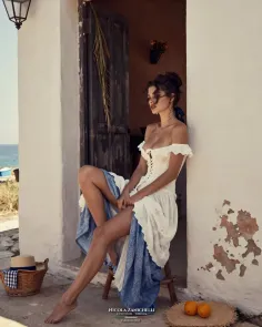 Woman in a white off-shoulder dress sitting outdoors with exposed legs