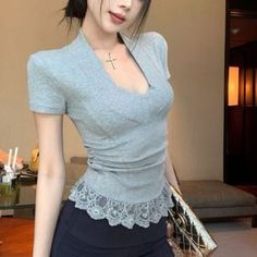 Woman in a grey top with lace trim and a cross necklace indoors