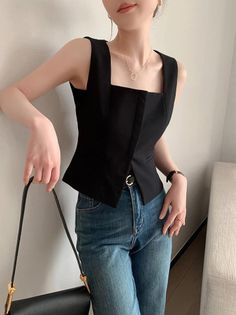 Woman in a black square-neck top and blue jeans holding a shoulder bag