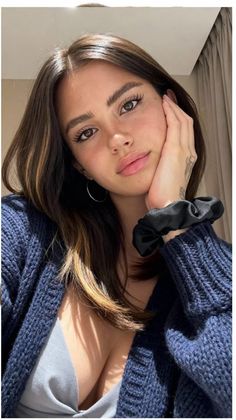 Woman with long dark brown hair wearing a blue cardigan and hoop earrings