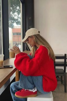 Woman in a red sweater and jeans drinking iced coffee at a cafe
