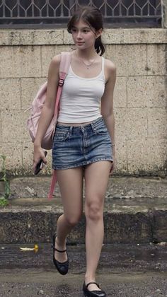 Young woman in a white tank top and denim skirt walking outdoors