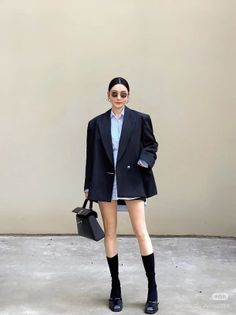 Woman in an oversized blazer, plaid shirt, and sunglasses holding a black handbag