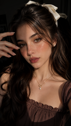 Woman with long brown hair and freckles wearing a brown top and gold necklace