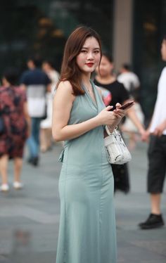 Woman in a light blue dress holding a phone on a busy street