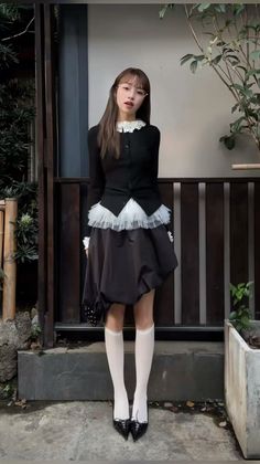 Woman in a black cardigan and bubble skirt with white knee socks and heels