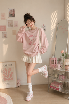 Woman in a pink sweatshirt and white pleated skirt posing indoors
