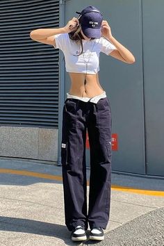 Woman in a white crop top and cargo pants with a baseball cap outdoors