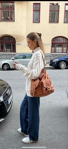 Woman in a white cable knit sweater and wide leg jeans on a street