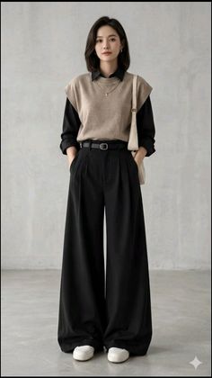 Woman in a black shirt, sweater vest, and wide leg pants standing indoors