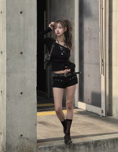 Woman in a black top and short shorts with a studded belt outdoors