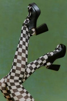 Legs in checkered tights and black platform heels against a green background