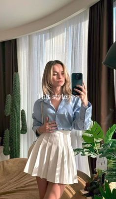 Woman in a blue shirt and white pleated skirt taking a mirror selfie