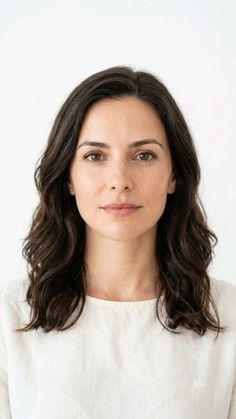 Woman with dark wavy hair in a simple white top against a white background
