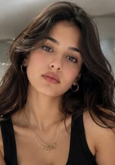 Woman with long dark hair wearing a black top and gold jewelry