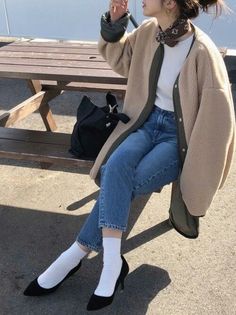 Person in a teddy coat, jeans, and heels sitting on a wooden bench outdoors