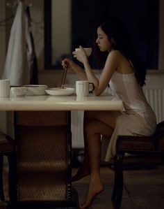 Woman with long dark hair eating at a table in soft, dark lighting