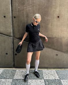 Woman in a black polo shirt and mini skirt with white knee socks and sunglasses