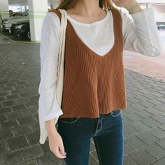 Person in a brown knitted top over a white long sleeve shirt and blue jeans
