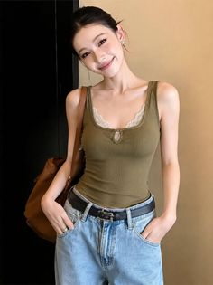 Woman in a green tank top with lace trim and blue jeans, smiling at the camera