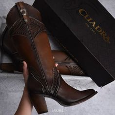 Brown leather cowboy boots with embossed details and a buckle, held by a hand