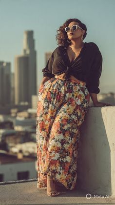 Woman in a floral skirt and black top on a rooftop with a cityscape background